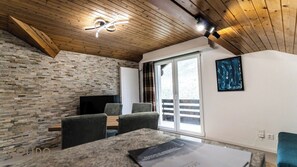 A room with a stone wall, wooden ceiling, a flat-screen TV, a sofa, and a painting.