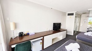 Quarto de hotel com escrivaninha, televisão, cama e pequeno espaço de cozinha.