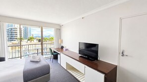 A hotel room with a bed, a desk with a television, a chair, and a view of the cityscape through large windows. - Cozy 2 Beds Hotel Room丨Beachside丨Max 4 guests (Surfers Paradise)
