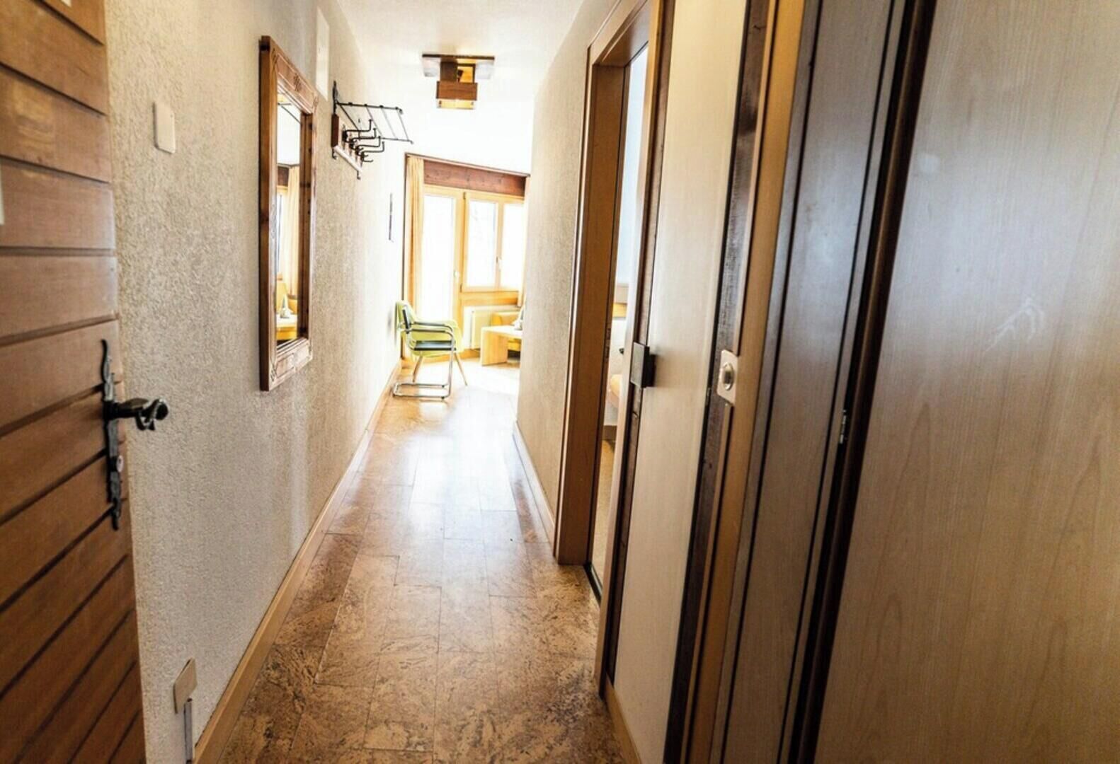 A hallway with wooden doors, a tiled floor, and a chair in the distance.