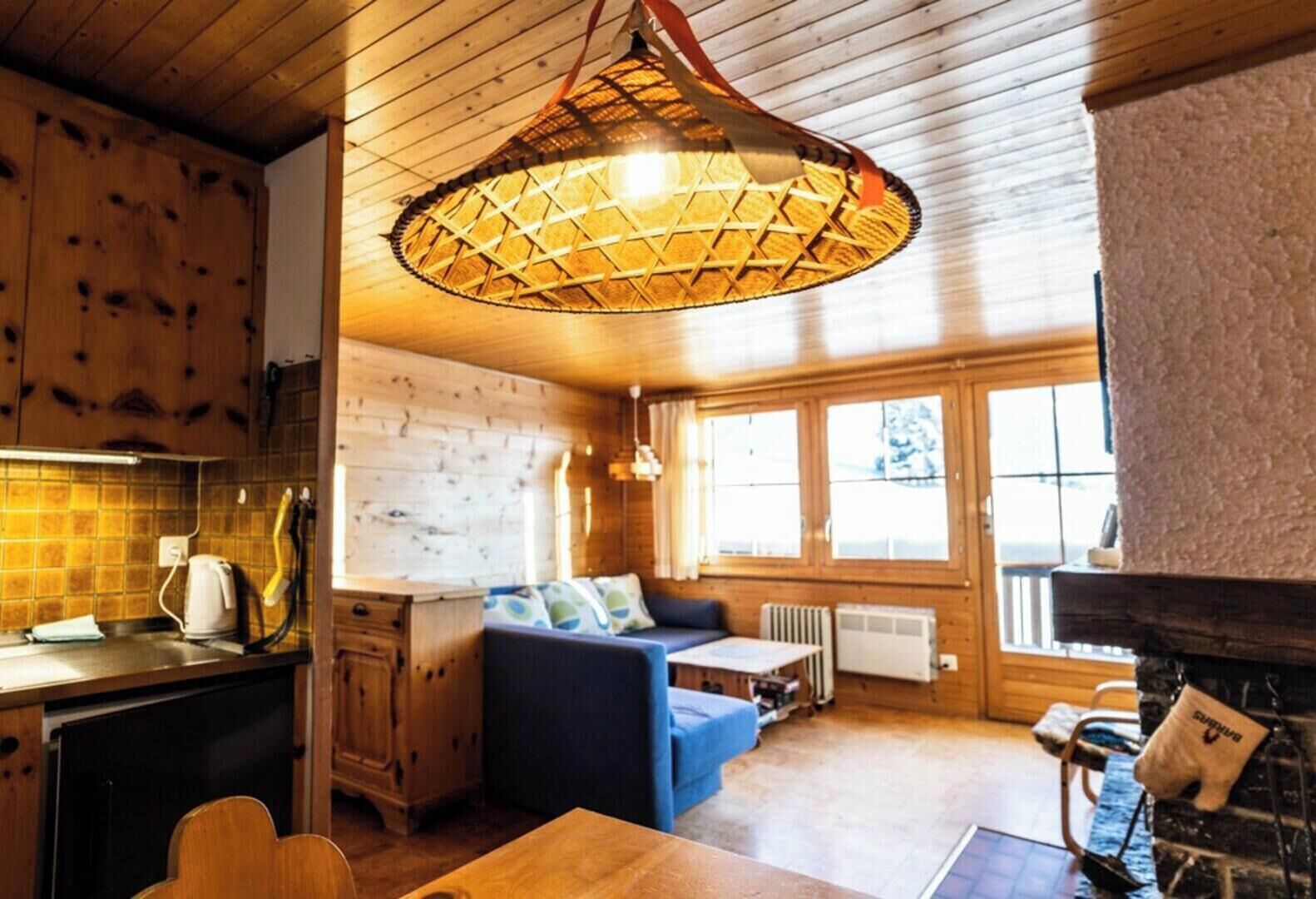 Een gezellig interieur van een chalet met een eethoek, een bank en een groot raam.