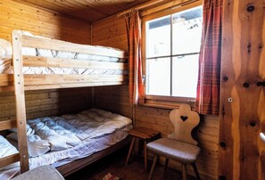 Ein Schlafraum mit Etagenbetten, einem kleinen Tisch, einem Stuhl, Holzwänden und einem Fenster mit Vorhängen.