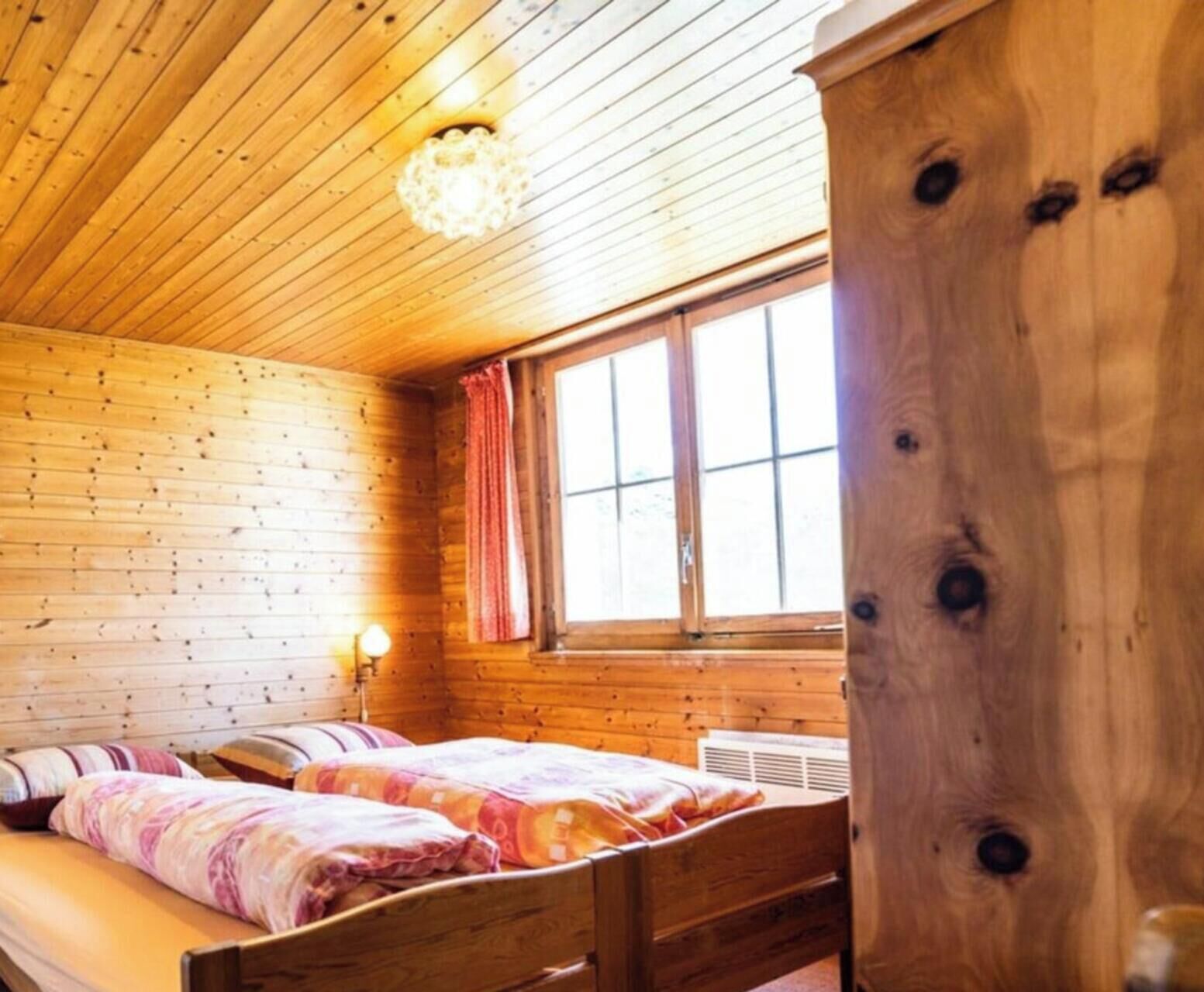Une pièce de cabane en bois comprenant un lit, une fenêtre avec des rideaux et un luminaire au plafond.