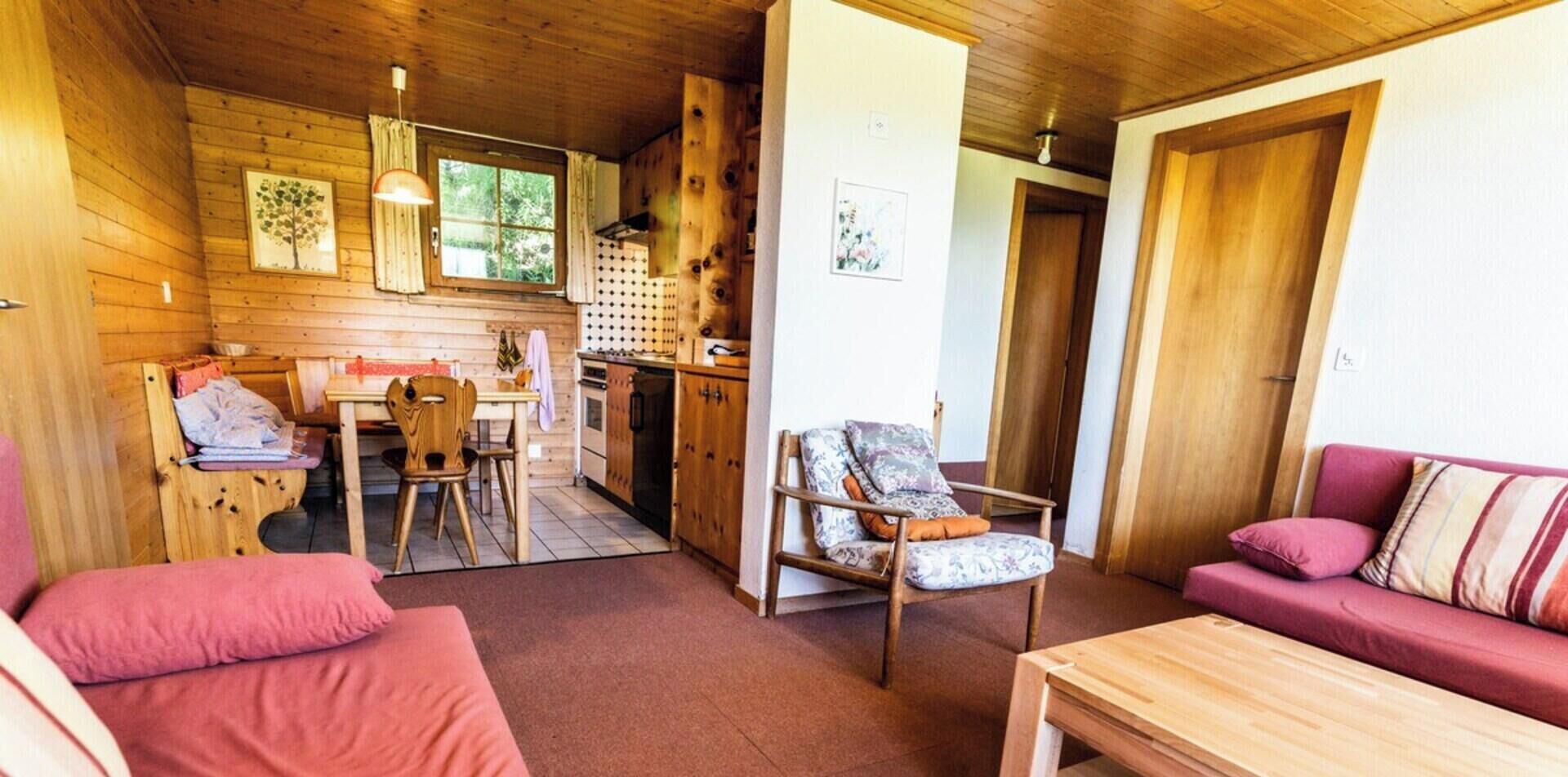 Ein gemütliches Blockhaus-Interieur mit Essbereich, einem Holztisch, einer Couch und einem Sessel.