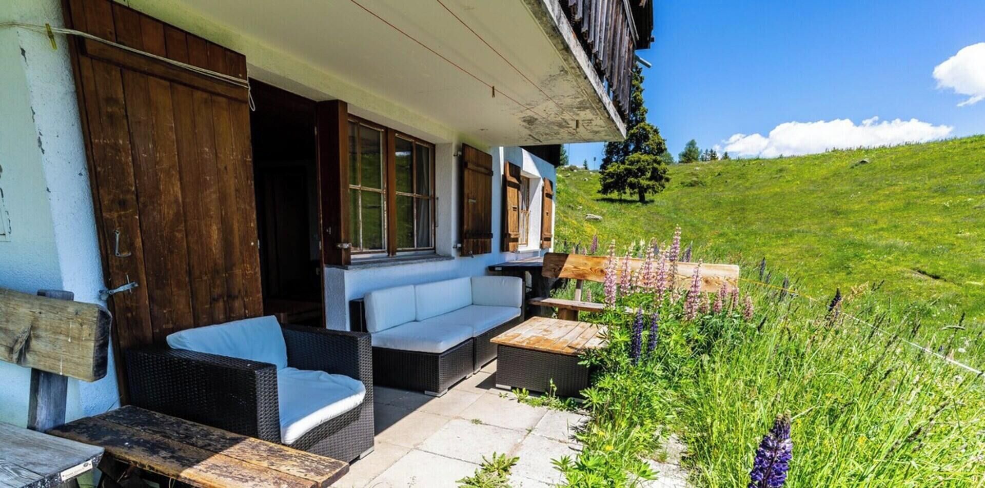 Un espacio de estar al aire libre cubierto con mobiliario de mimbre y una mesa de madera, con vistas a una ladera cubierta de hierba.