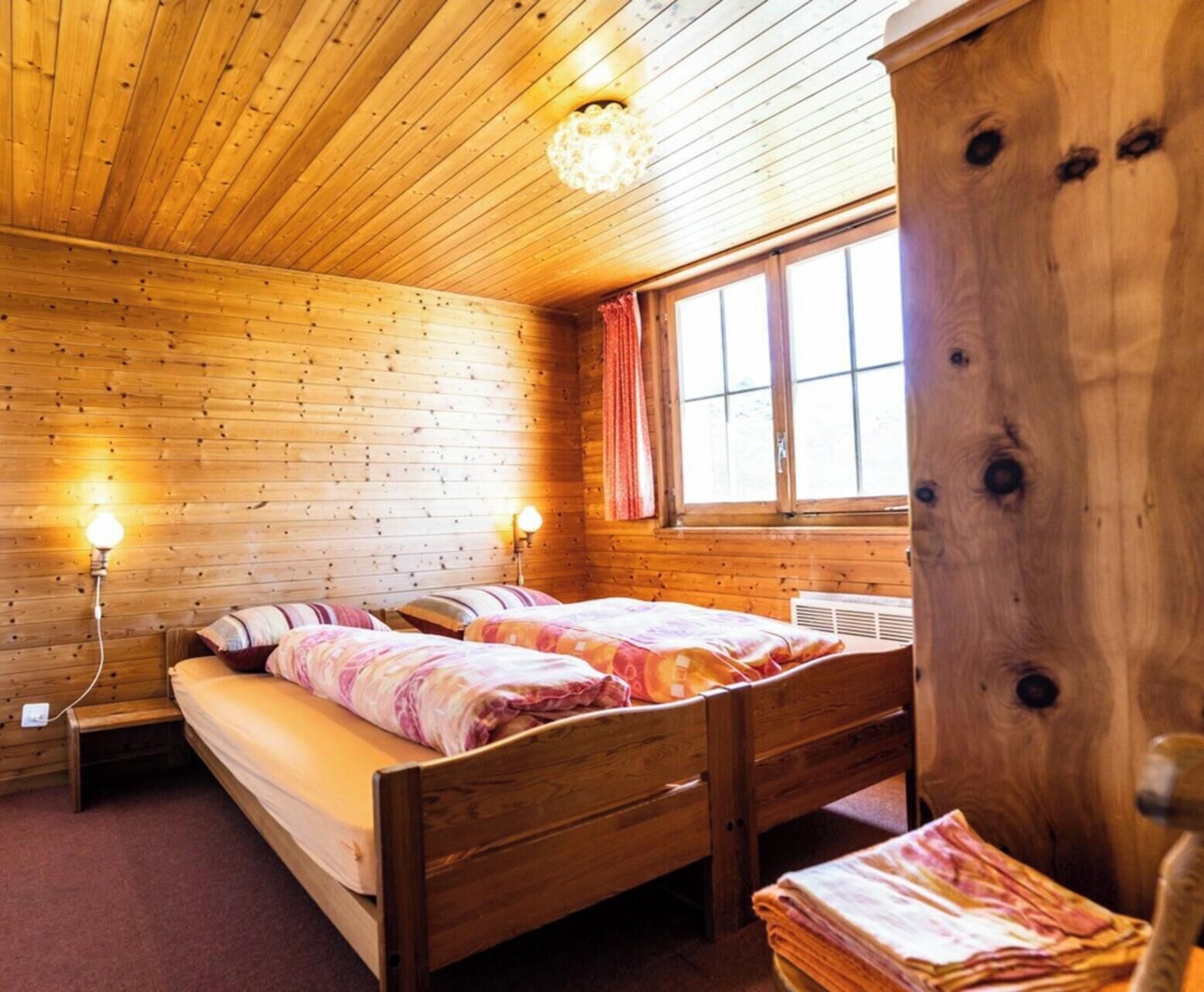 Ein Zimmer in einer Holzhütte mit zwei Betten, einem fenster mit Vorhängen und einem Holzschrank.