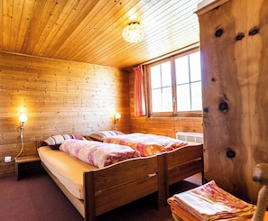 Ein Zimmer in einer Holzhütte mit zwei Betten, einem fenster mit Vorhängen und einem Holzschrank.