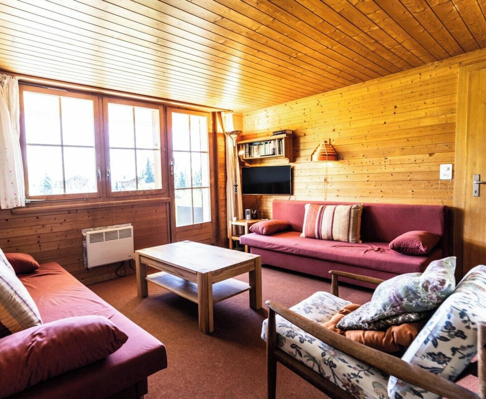 Interior acogedor de una cabaña con techo de madera, un sofá, una mesa y un televisor.