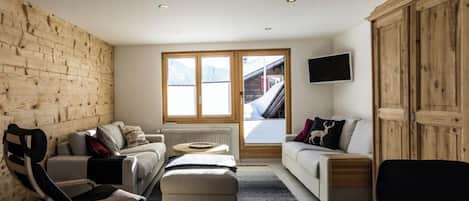 A modern living room with a wooden accent wall, a sofa, a chair, a television, and a view of a ski lift.