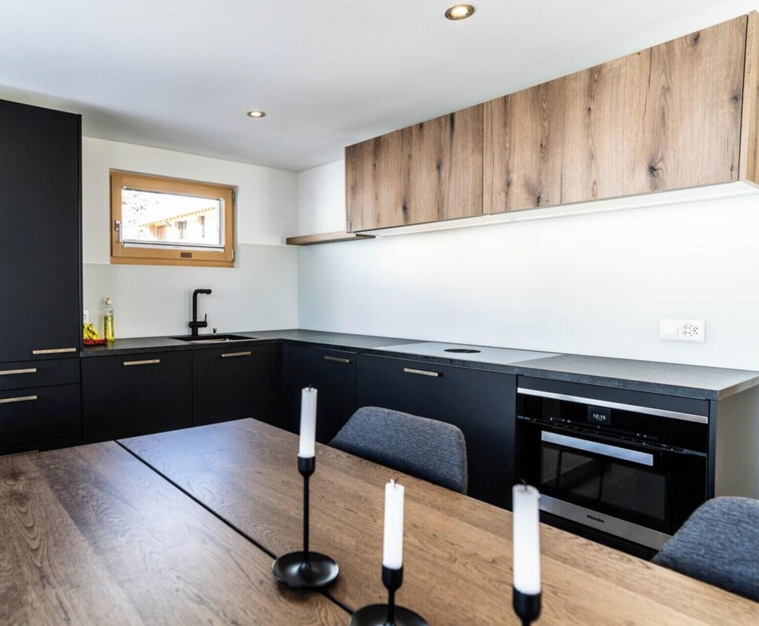 A modern kitchen with dark cabinetry, a wooden countertop, and a built-in oven.