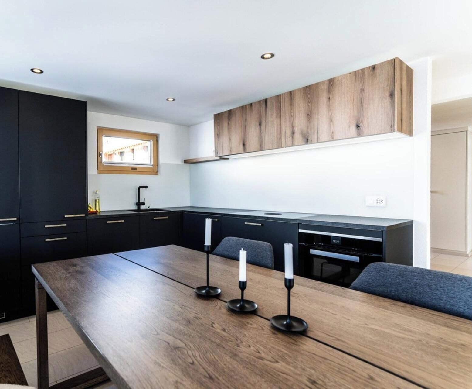 Una cocina moderna con muebles oscuros, una mesa de comedor de madera y un horno empotrado.