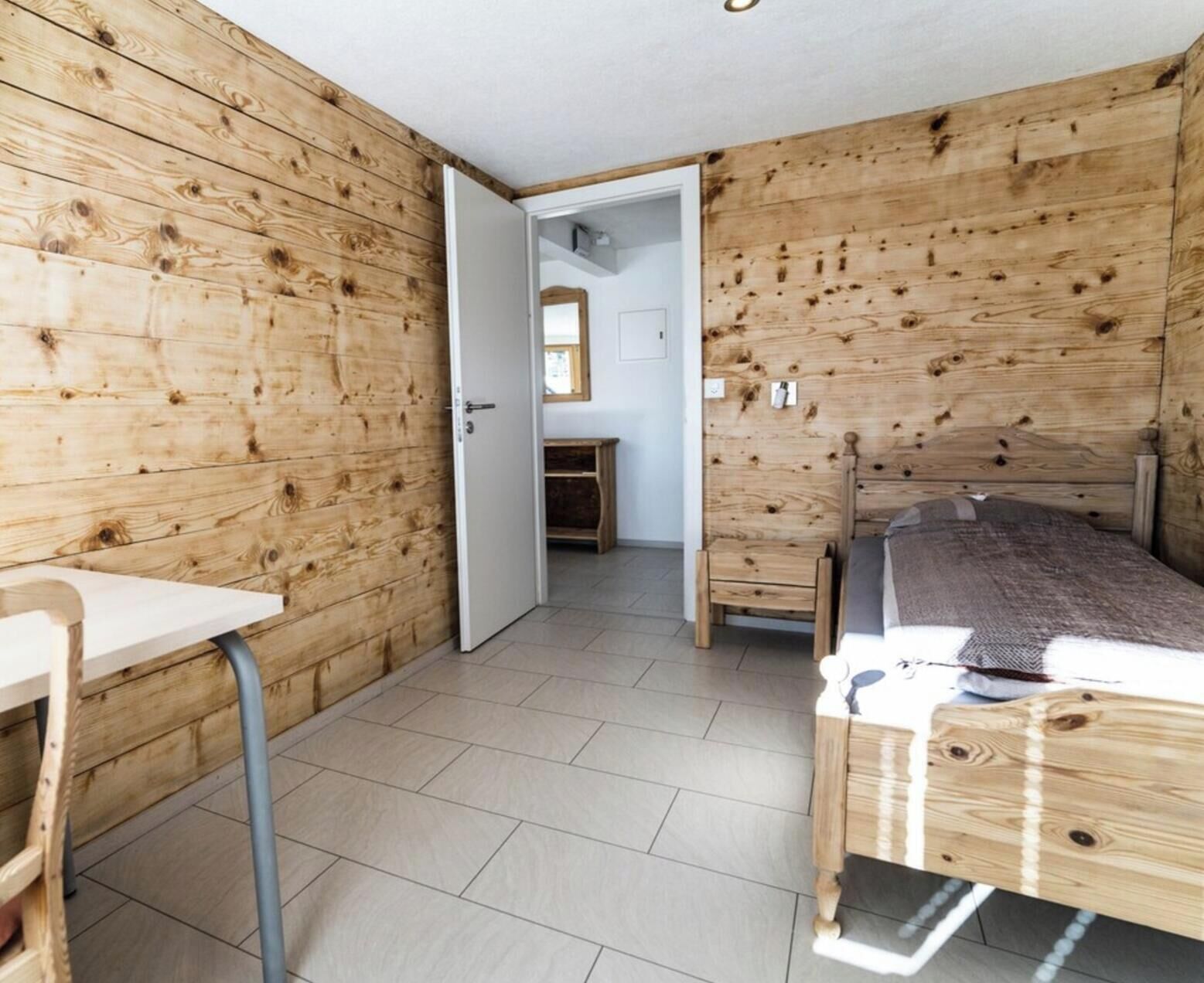 Quarto com paredes de madeira, uma cama, uma escrivaninha e uma cadeira.