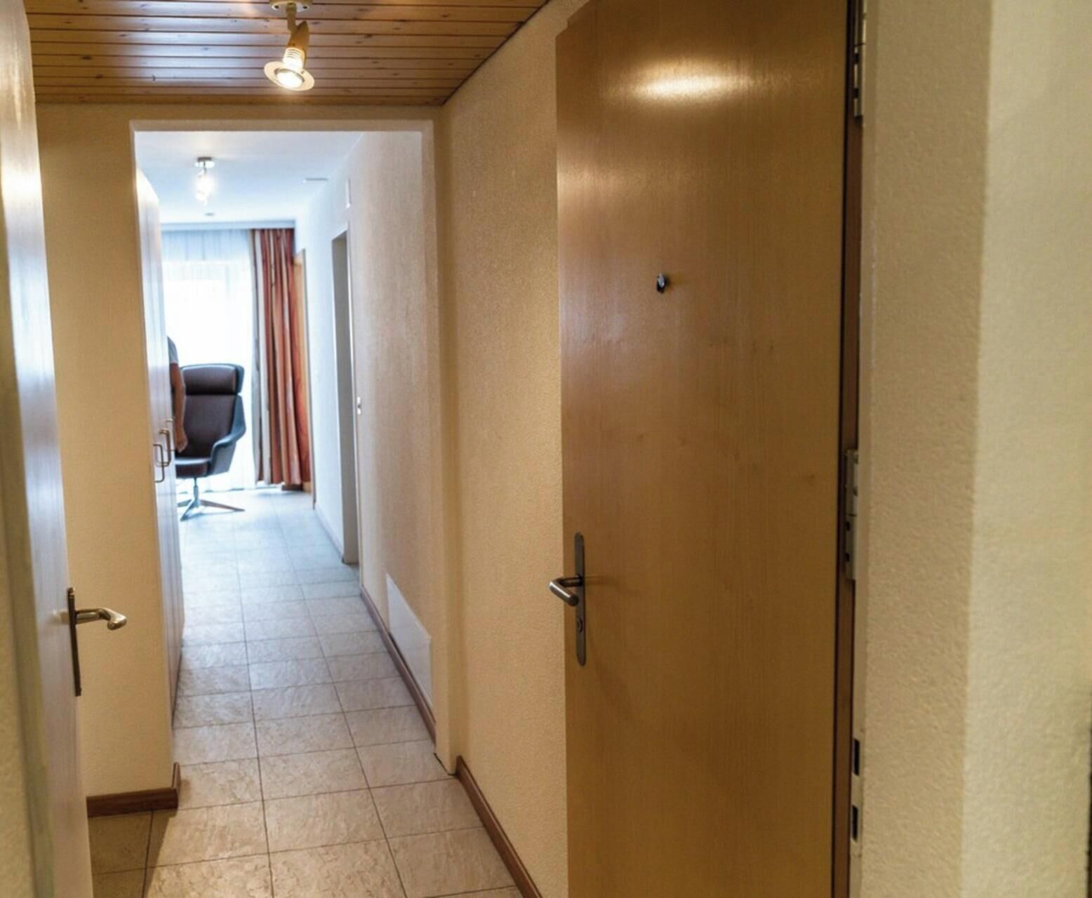 Un couloir avec une porte fermée, une chaise et une fenêtre avec des rideaux.