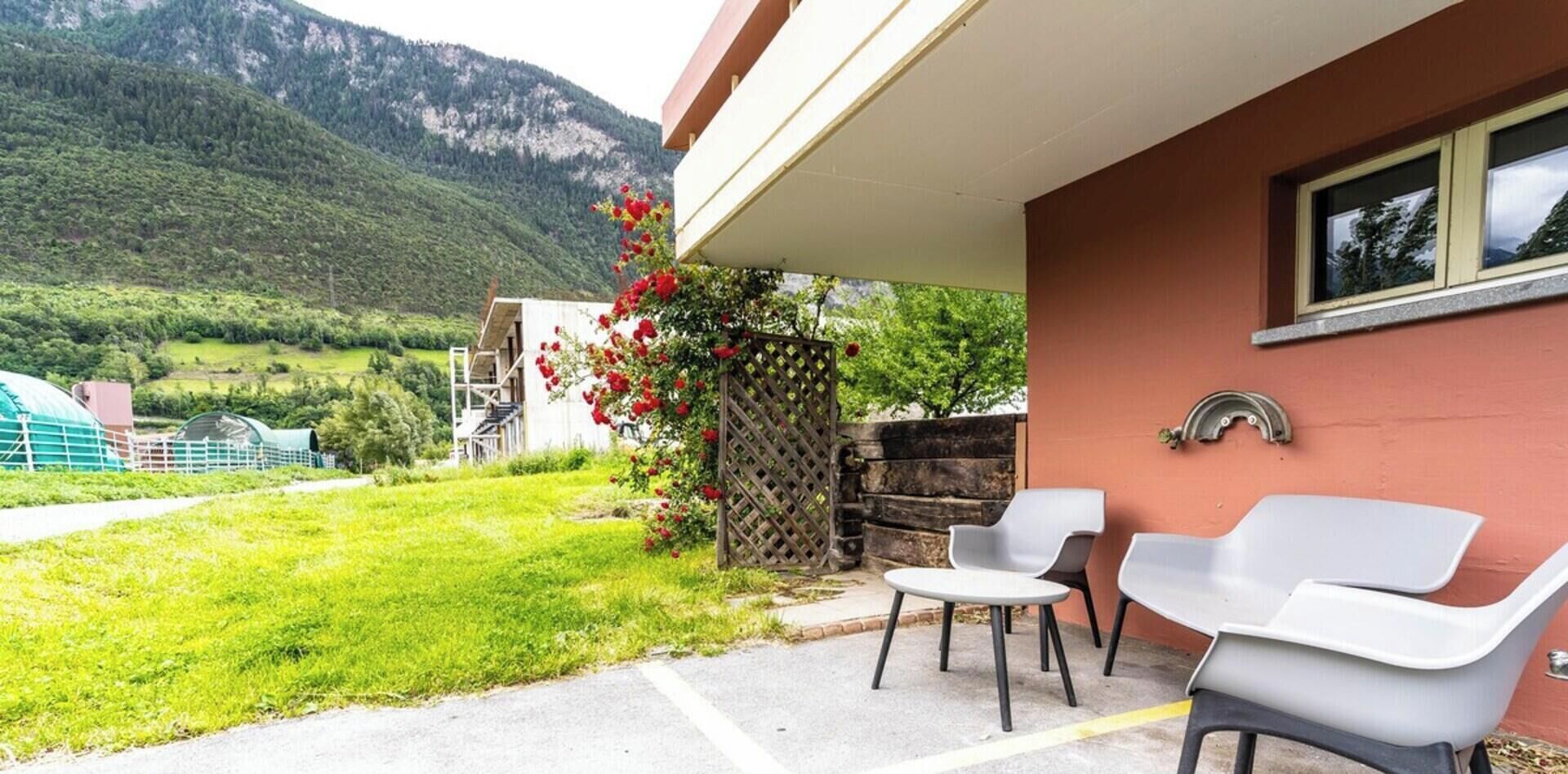 Une terrasse avec des sièges extérieurs, une vue sur une montagne et un bâtiment doté d’un mur rouge.