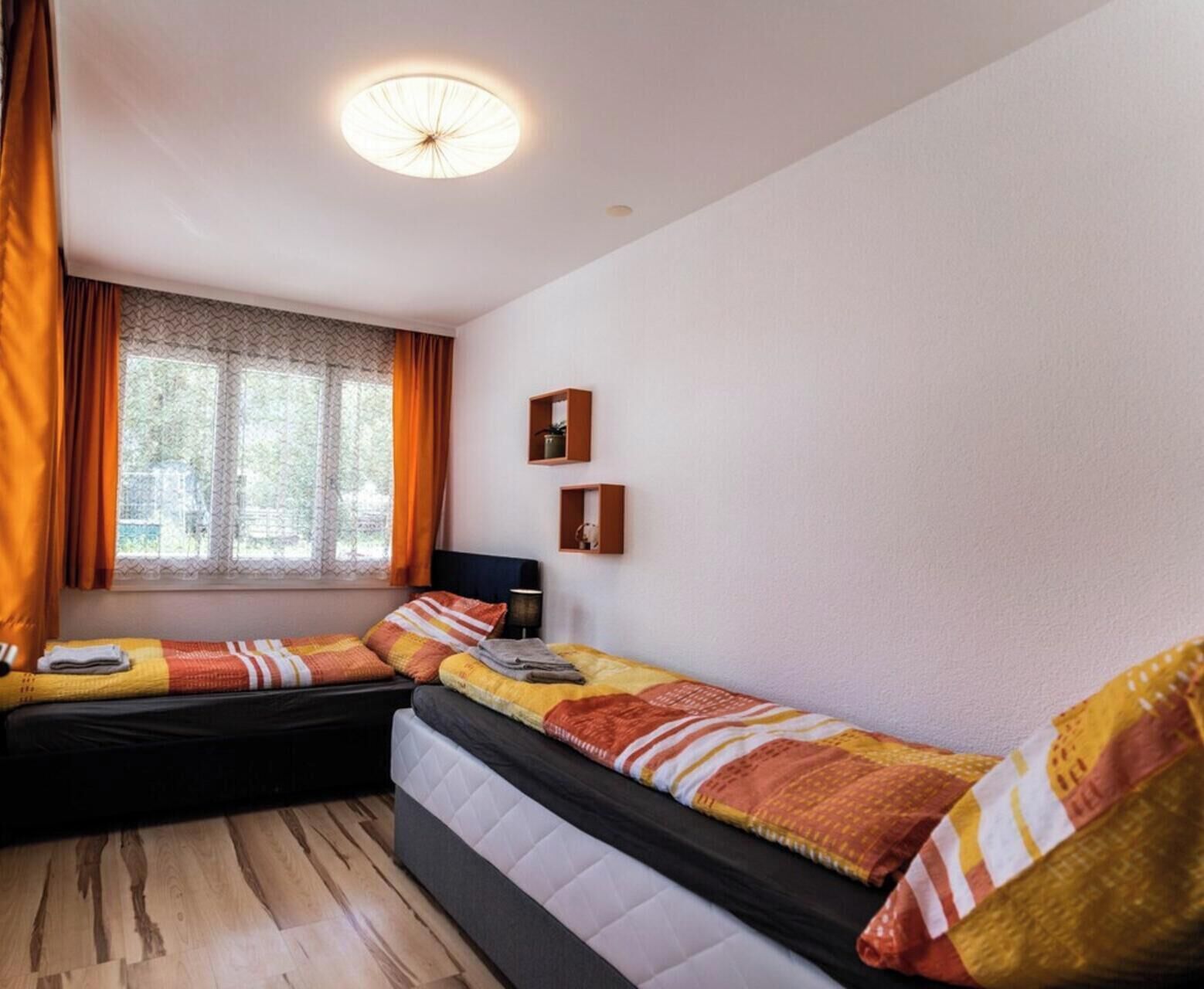 Une chambre avec deux lits, une fenêtre avec des rideaux, une petite table et une étagère fixée au mur.