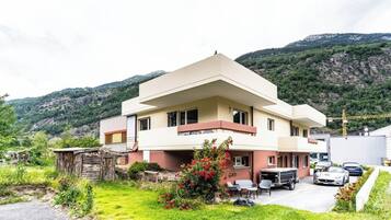 Un bâtiment à deux étages, doté d’un toit plat, d’un balcon à l’étage supérieur et d’un petit jardin agrémenté de fleurs rouges.