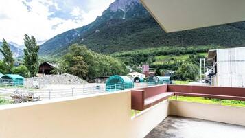 Un balcon donnant sur un paysage montagneux, une tente verte et un bâtiment doté d’un toit en pente.