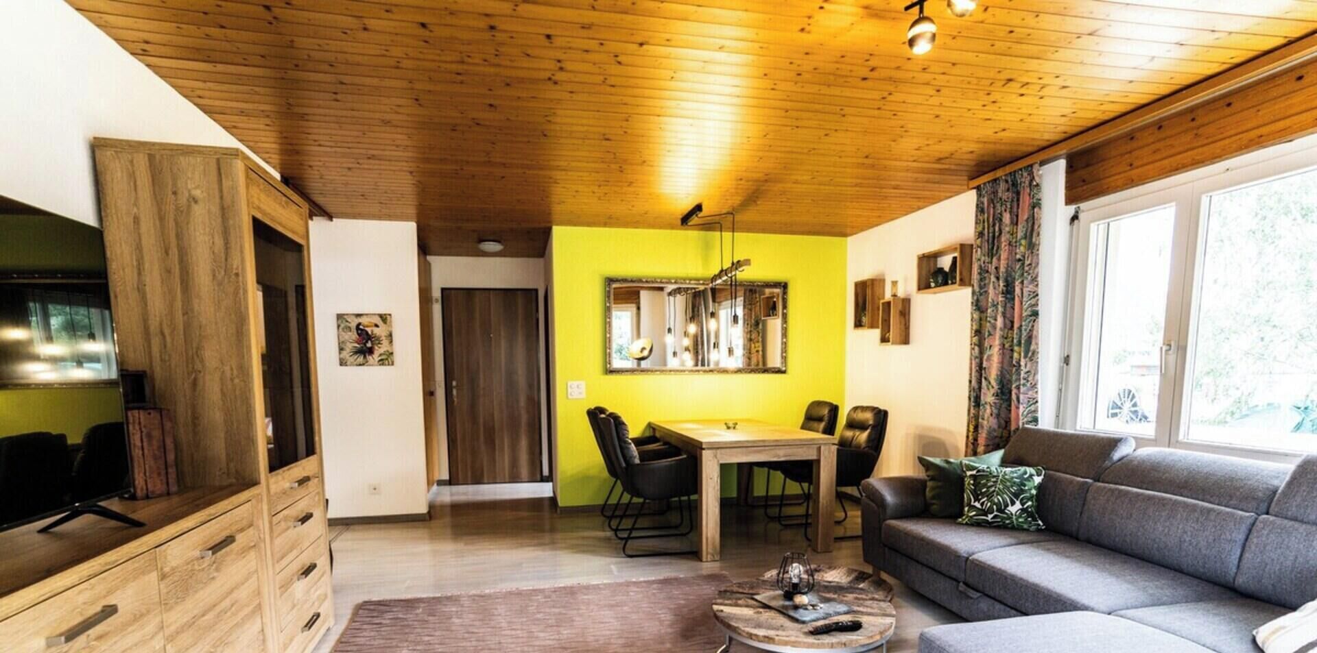 Un salon chaleureux avec un coin repas, un plafond en bois et une grande fenêtre.