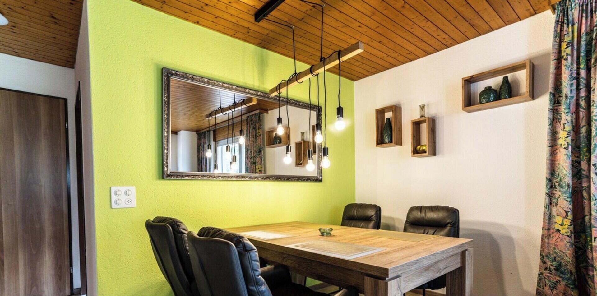 Un coin repas comprenant une table en bois, quatre chaises, un miroir, des luminaires suspendus et un plafond en bois.