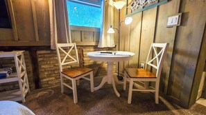 Una habitación acogedora con dos sillas blancas, una pequeña mesa redonda y una ventana con cortinas.