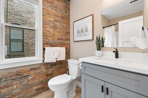 Ein Badezimmer mit Ziegelwand, Toilette, Waschbecken mit Spiegel und einem gerahmten Bild an der Wand.