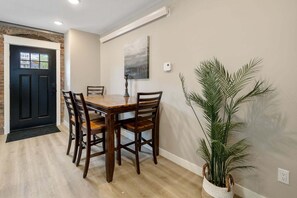 Ein Essbereich mit Holztisch und -stühlen, einer schwarzen Tür, einer Wandklimaanlage und einem Blumentopf.