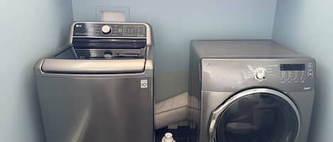 Un espace buanderie compact comprenant un lave-linge et un sèche-linge, tous deux en acier inoxydable, ainsi qu’une bouteille de détergent Purex.