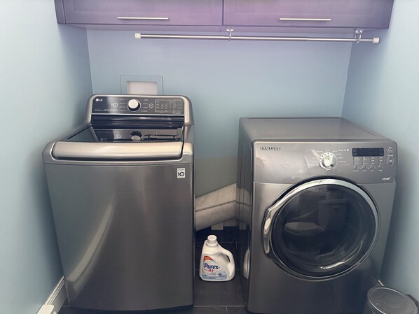 A compact laundry area with a washing machine and a dryer, both in stainless steel, and a bottle of Purex detergent.