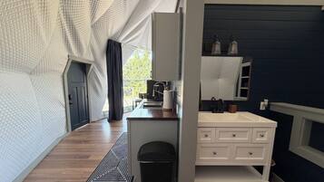 A modern bathroom with a white vanity, a mirror, and a sink. There is a black trash bin and a patterned rug on the floor.