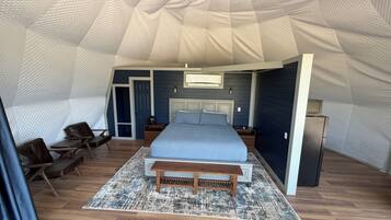 A tented accommodation with a bed, seating area, and a small kitchenette.
