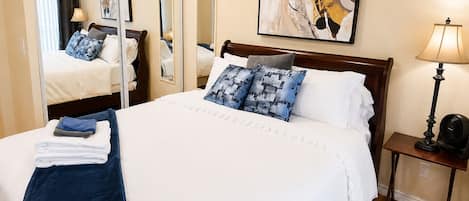 A hotel room with a large bed, a bedside table with a lamp, a mirror, and a painting on the wall.