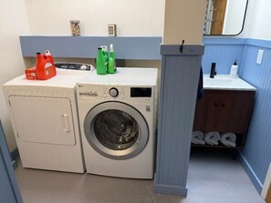 Ein kleiner Waschraum mit Waschmaschine und Trockner, einem Regal für Reinigungsmittel und einem Waschbecken mit Unterschrank.