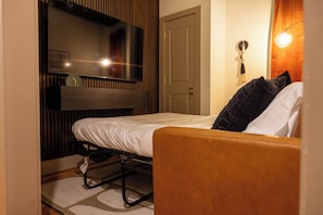 Une chambre à coucher comprenant un lit, un téléviseur fixé au mur, une porte et un luminaire fixé au mur.