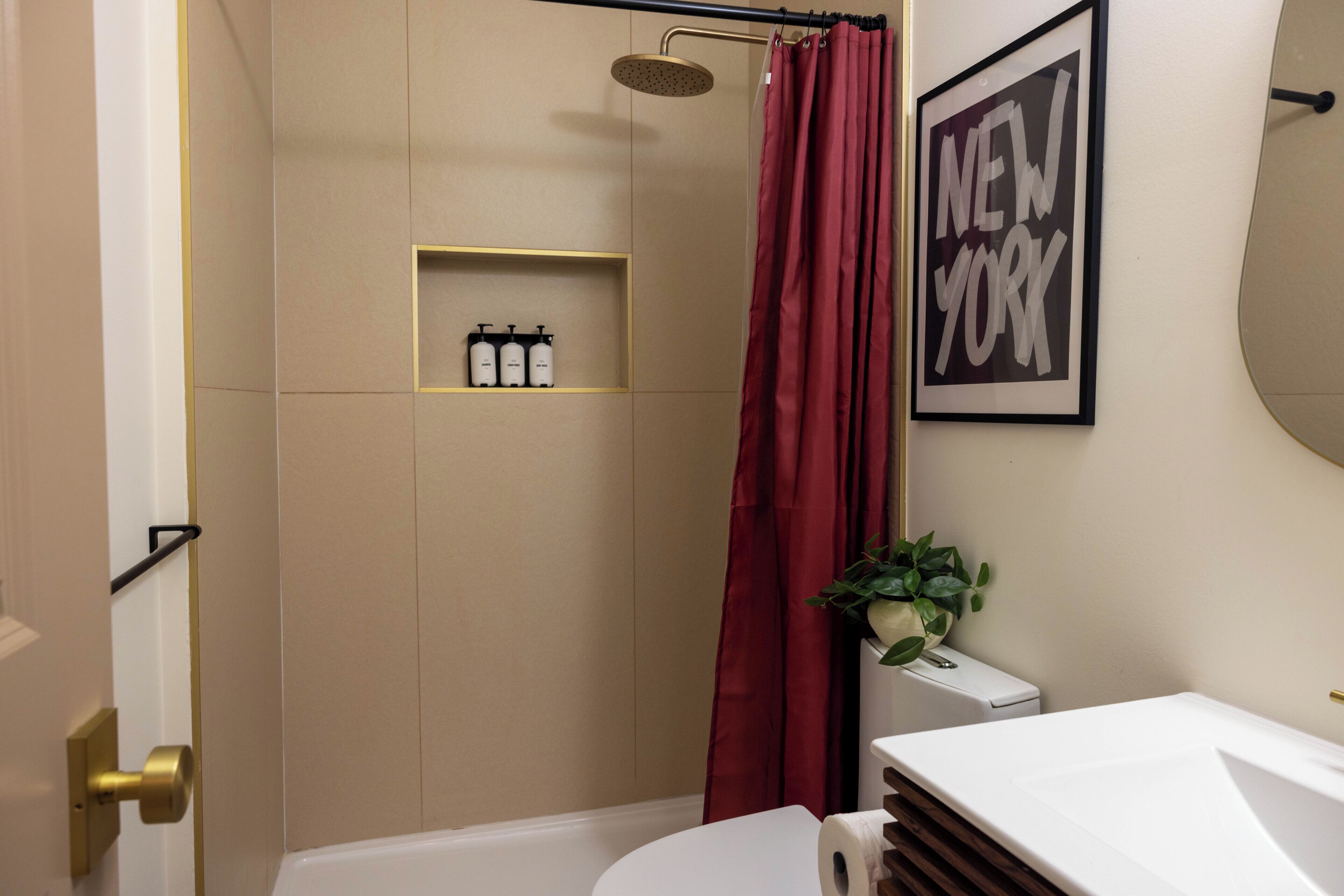 A modern bathroom with a shower, a toilet, and a sink. There is a shelf with toiletries and a framed picture on the wall.