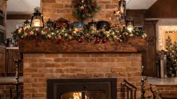 Une cheminée avec un manteau en briques, un feu de bois et une couronne de Noël.