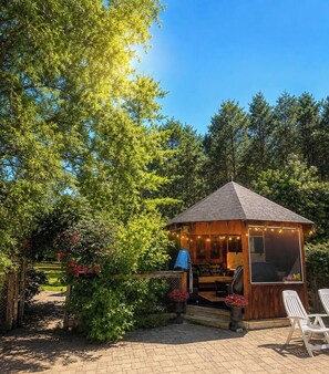 A wooden cabin with a porch, surrounded by greenery and trees.
