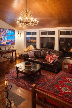 A cozy living room with a leather sofa, a glass coffee table, and a chandelier.