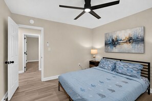 A bedroom with a bed, a ceiling fan, a nightstand with a lamp, and a painting on the wall. - Modern Furnished Home Near CLT Airport (Charlotte)