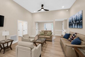 A spacious living room with a high ceiling, a ceiling fan, and a cityscape painting on the wall. - Modern Furnished Home Near CLT Airport (Charlotte)