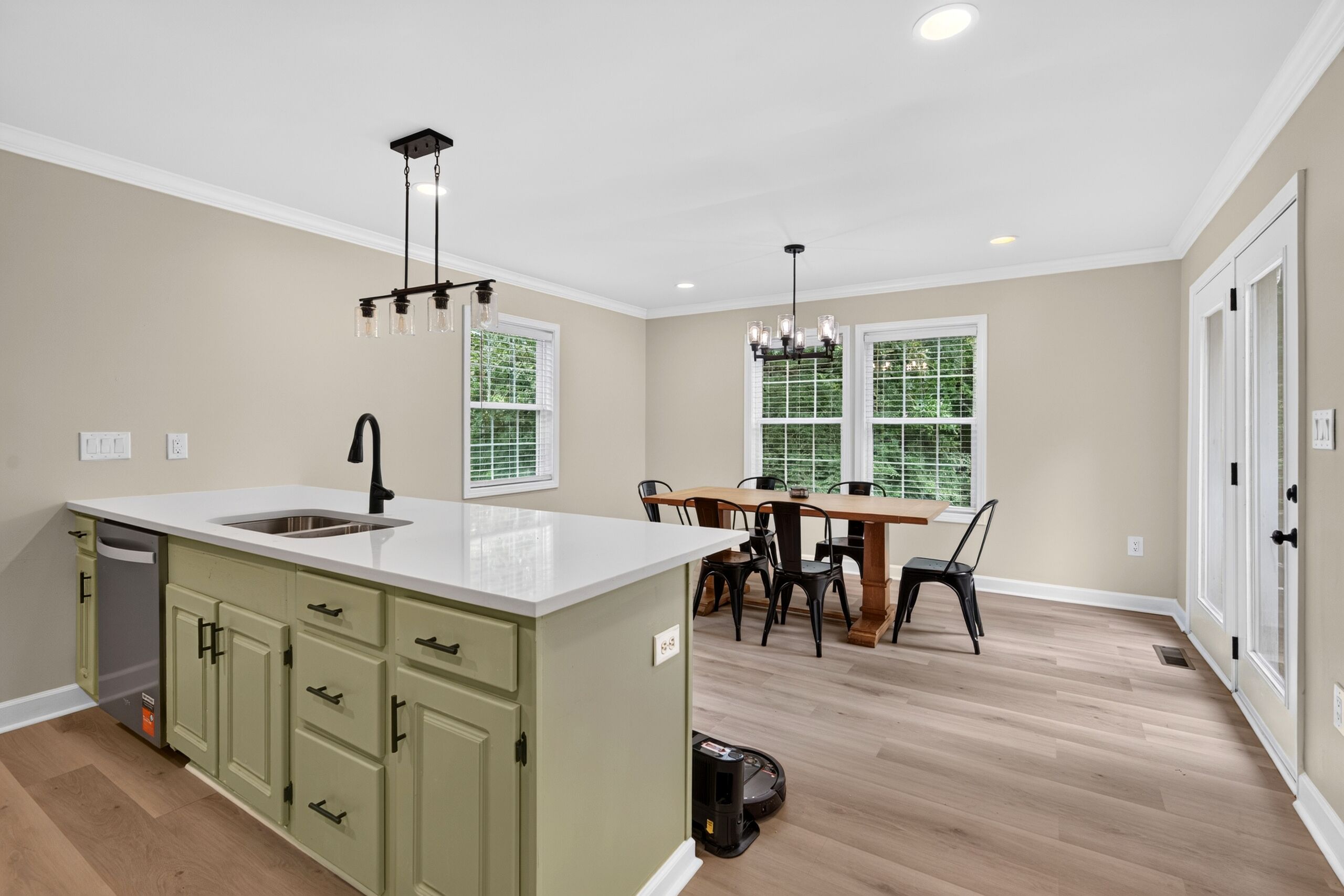 A modern kitchen with a central island, a dining area with a wooden table and chairs, and large windows with blinds.