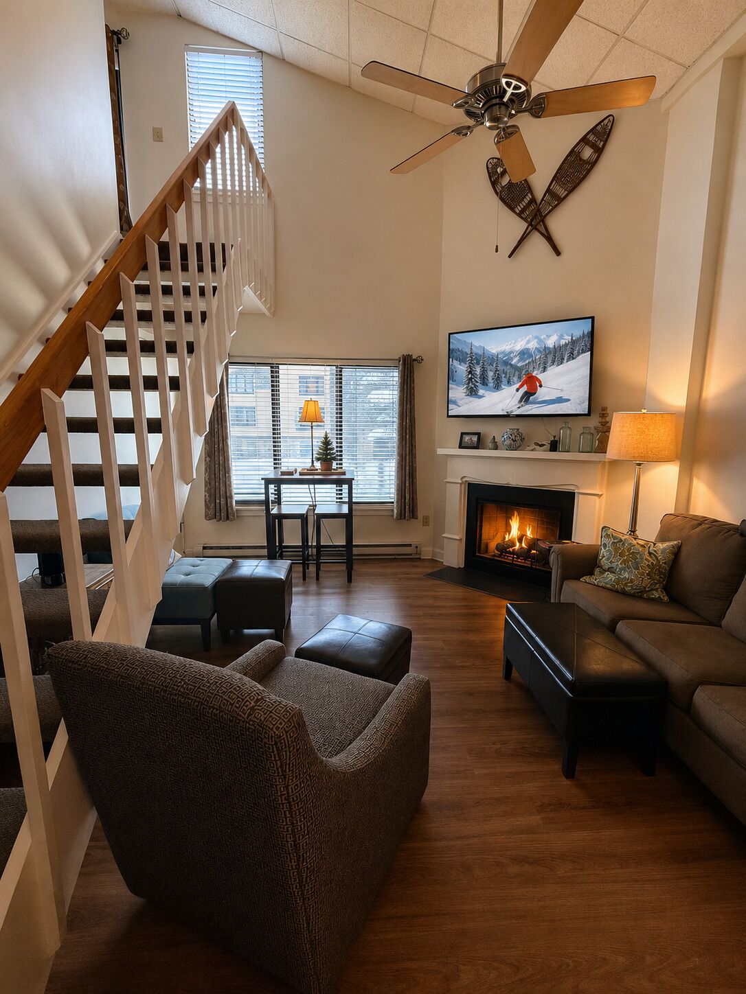 A living room with a fireplace, a television mounted on the wall, a ceiling fan, and a staircase.