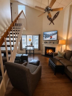 Ein Wohnzimmer mit Kamin, Wandfernseher, Deckenventilator und einer Treppe.