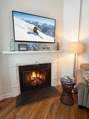 Ein Wohnzimmer mit Kamin, einem darüber hängenden Fernseher und einem Beistelltisch mit Büchern.