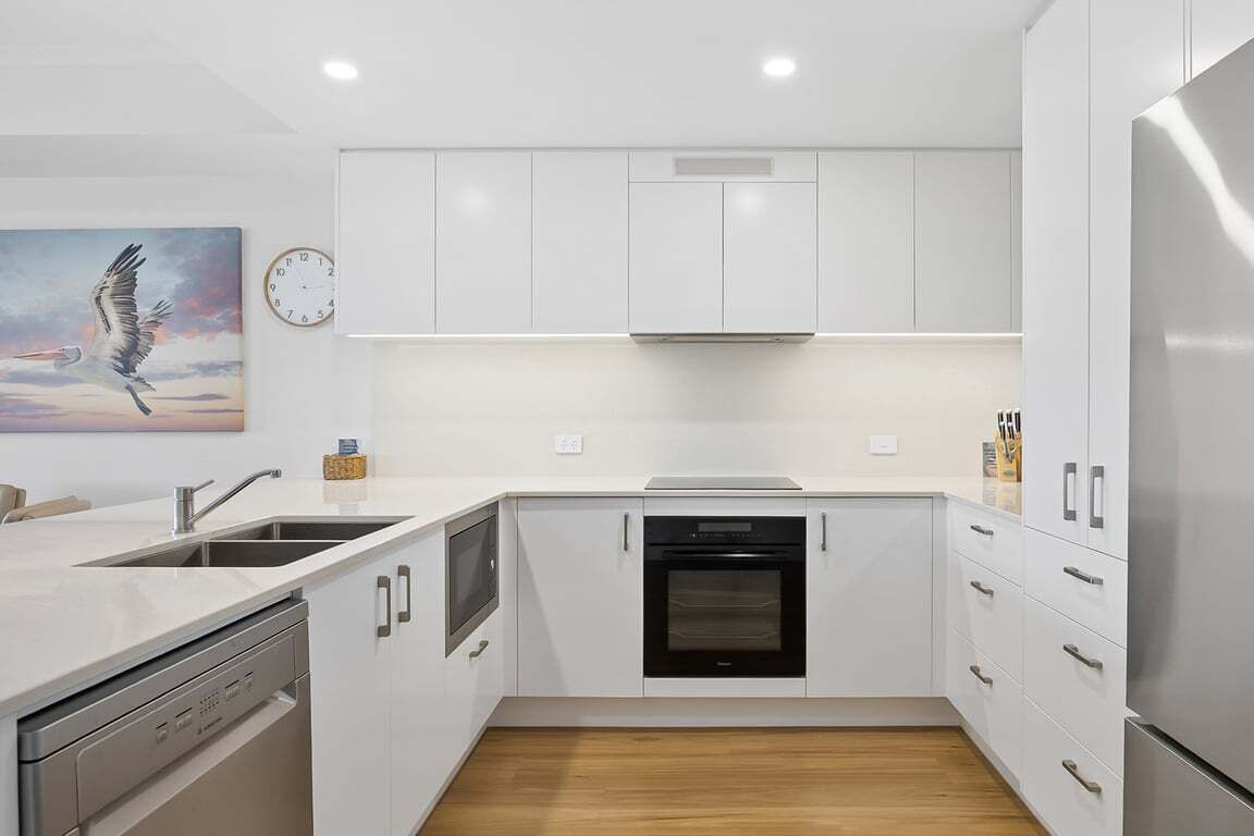 A modern kitchen with white cabinetry, a built-in oven, and a stainless steel refrigerator.