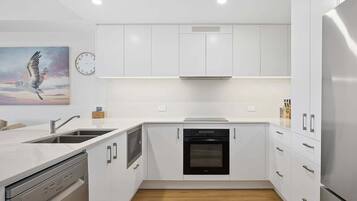 A modern kitchen with white cabinetry, a built-in oven, and a stainless steel refrigerator.