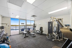 A gym with various exercise equipment, a large window with a view of a body of water, and a ceiling with recessed lighting.