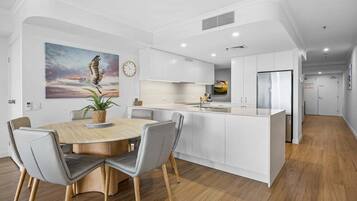 A modern kitchen with white cabinetry, a central island, and a dining area with a wooden table and grey chairs.