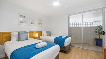 A hotel room with two beds, a ceiling fan, and a sliding glass door leading to a balcony.