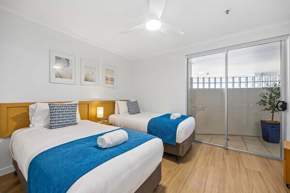 A hotel room with two beds, a ceiling fan, and a sliding glass door leading to a balcony.