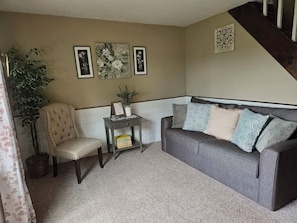 A living room with a grey sofa, a beige armchair, a small table with a plant, and framed artwork on the wall.